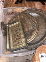 Metal trays and metal wall art photographed together in a plastic bin showing intricate Egyptian designs and patina finish.