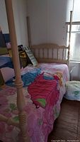 Wood twin bed frame with spindle headboard and footboard; colorful bed linens with floral and character print visible