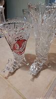Two vintage crystal vases on tiled floor, one with a red bird decorative accent and both with bird figurine feet as base.