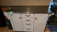 Front view of the white wood kitchen cart showing four drawers and two cupboard doors with black handles and a stainless steel top.