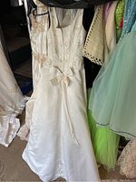 White gowns with embroidered bodices and satin skirts on hangers and folded on floor