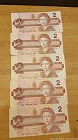 Front side of five 1986 Canadian $2 bills arranged vertically, showing Queen Elizabeth II portrait and denomination