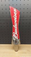 Front view of a Budweiser beer draft handle showing red upper section with white Budweiser script and chrome lower base.