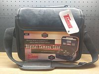 Front view of the black leather Targus digital camera case with original tag, showing the product label and adjustable shoulder strap.