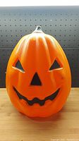 Front view of orange pumpkin blow mold showing carved jack-o'-lantern face with triangular eyes, nose, and jagged mouth.