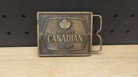 Front view of Molson Canadian Lager belt buckle showing embossed maple leaf and text logo