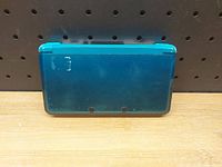 Closed view of turquoise blue Nintendo 3DS handheld showing top cover with some scratches and wear.