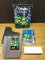 Full set of Othello NES game including cartridge, box, manual and styrofoam insert displayed on a table against pegboard backdrop.