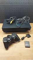 Full set shown on wooden surface with PlayStation 2 console, controller wrapped around cable, memory card in front, and cables on top of console.