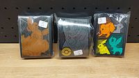 Front view of three sealed packs of Pokemon card sleeves with different character designs visible through clear packaging.