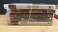 Stack of five PS3 games including Assassin's Creed II, BioShock, Skyrim, Prince of Persia, and Call of Duty Modern Warfare 3.