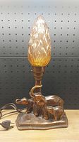 Front view of vintage lamp showing three elephant base and amber glass shade with visible chip.