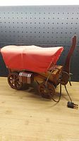 Side view of the vintage wooden wagon light displaying the red fabric canopy, wooden wheels, and electrical cord with plug.