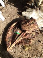 Folded large nylon camouflage cover laying on dirt ground.