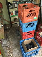 Photo showing stacked plastic milk crates on metal hand cart in a basement or storage area with concrete floor and shelves in background