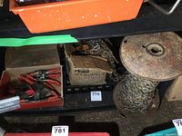 Box containing multiple red-handled spring clamps on a black shelf with a nearby chain hoist box and chain spool.
