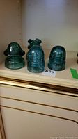 Four turquoise glass insulators on shelf, three shown with different shapes and sizes