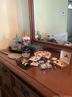 Wide view of all items on wooden surface in front of mirror including jewellery, watches, perfume bottles and vanity mirror.