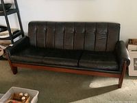Full front view of black leather sofa with teak frame