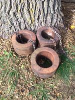 Three large old motor windings stacked and chained beside a tree on dry leaf ground.