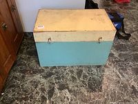 Closed wooden tool chest painted blue-green and yellow, showing wear and tear.