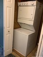 Full view of white stacked washer and dryer in plywood enclosure