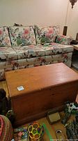 Solid wood blanket chest in front of floral sofa and surrounded by toys and other items on the floor.