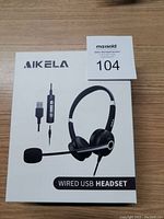 Box front showing Aikela branding, image of the wired USB headset with inline control.