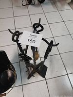 Photo showing fireplace tool stand with poker, tongs, brush, and shovel tools, and black bucket beside it on tiled floor.