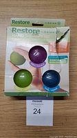 Front view of the Gaiam Restore Hand Therapy Kit with three therapy balls in green, purple, and blue visible through open and distressed packaging.
