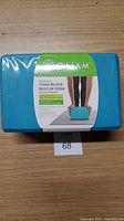Front view of the yoga block in packaging showing the blue face with product label indicating 'Tri-Colour Yoga Block' by Gaiam.