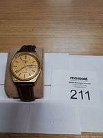 Front view of the gold-tone Pulsar wristwatch showing the dial, hour markers, day/date window, and brown leather strap on a cuff.