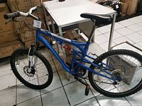 Side view of blue Wicked brand mountain bike frame showing full profile including front and rear suspension, knobby tires, and pedals.