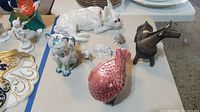 Overview photo of all five animal figurines including cat, dog, lamb, horse, and pink bird on table.