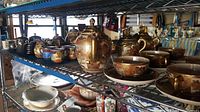 Overall view on wire shelving showing multiple tea set pieces including Satsuma-style, brown cups, gold-red pots