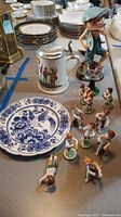 Wide view showing multiple porcelain figurines, a blue and white decorative plate, and a German beer stein with pewter lid.