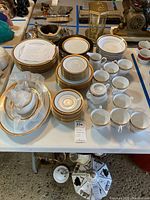 Full set displayed on table showing multiple plates, cups, bowls, creamers, and sugar bowl with lids, featuring gold rim decoration.
