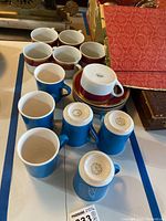 Six blue Syracuse China mugs, some upright and some upside down showing branded stamps on the bottom, arranged on a table.