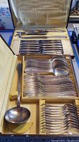 Overall view of two yellow-gold storage boxes containing multiple pieces of silver plated cutlery and serveware including ladle, forks, spoons, carving set.
