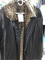 Front view of black leather jacket showing leopard print lining and collar, with visible buttons and front pockets.