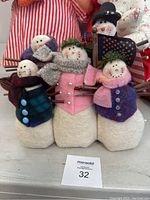 Five plush snowman figures in multicolored coats and scarves, wooden twig arms, with one holding an American flag and a black top hat.