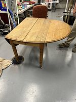Full view of antique oak drop-leaf table with one leaf extended showing round edge and turned legs.