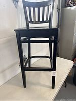 Front view of black wooden bar stool showing seat and slatted backrest