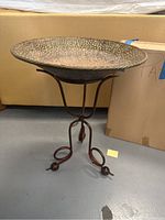 Hammered metal shallow bowl bird bath on decorative metal stand with curled feet and ball accents.