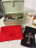 Photo showing green jewelry box with watches, and pouches including red fabric and black pouch with cross pendant