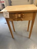 Front side view of unfinished wooden end table with decorative bow.