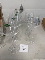 Eight Shannon crystal wine glasses, four with plain clear bowls and green Shannon crystal logos, two with snowflake designs, displayed on a shelf.