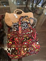 Photo showing a beige woven handbag, a multicolor patterned Vera Bradley fabric handbag, and a black and white handbag with heart charm detail.