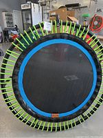 Top-down view of the heavy duty Bellicon exercise trampoline showing the black mat, blue ring, and bright green elastic suspension bands attached to the circular frame.