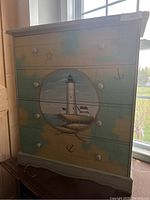 Front view of wooden chest showing painted lighthouse scene on drawers.